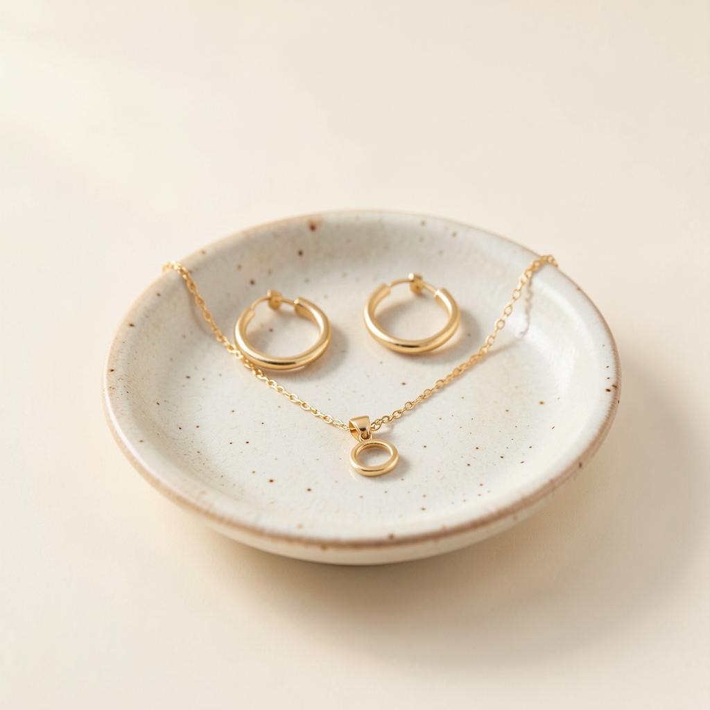 Gold hoop earrings and pendant necklace on a ceramic dish